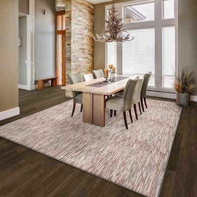 Dining area with a a pink beige and grey area rug over the wooden table and taupe chairs. large windows in the background with white blinds.